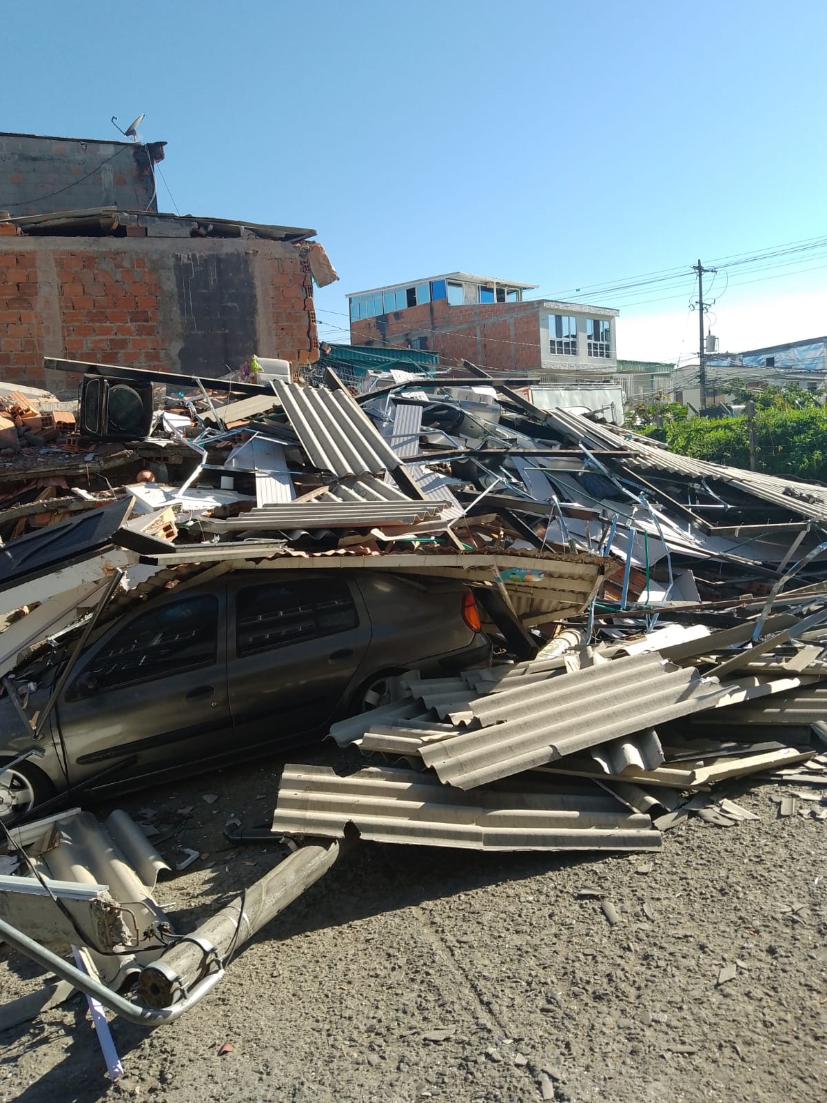 Collapsed construction materials and a vehicle trapped beneath debris.